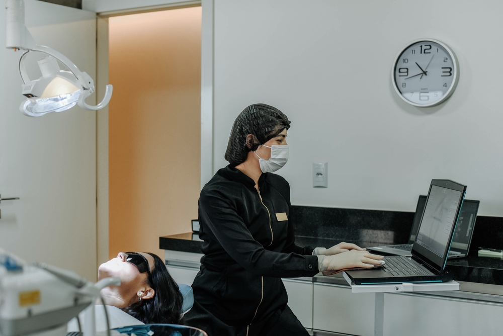 Dentist typing on computer while preparing for a dental procedure to improve AI visibility and digital presence
